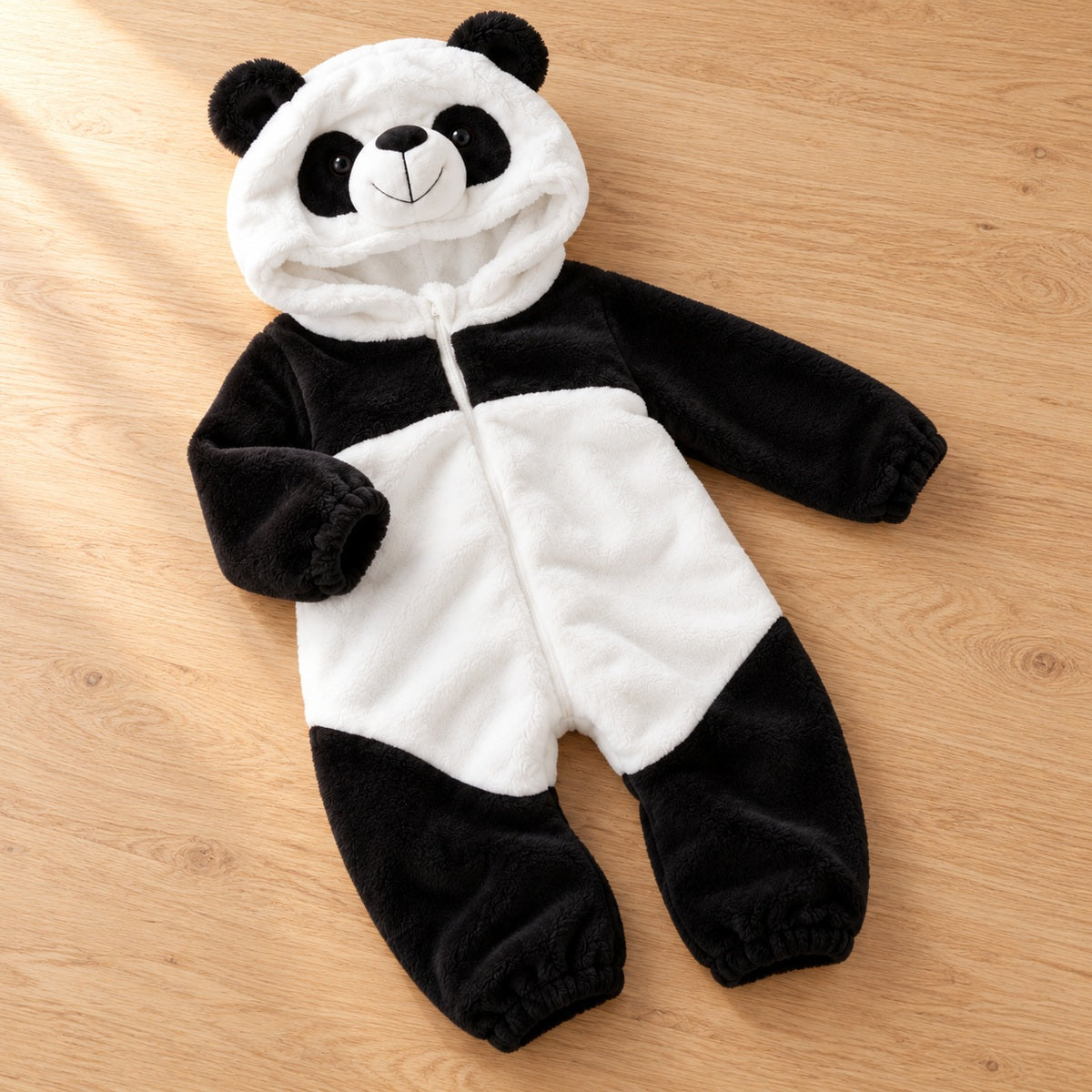 Full black and white panda hooded romper laid casually on a light natural wood surface.